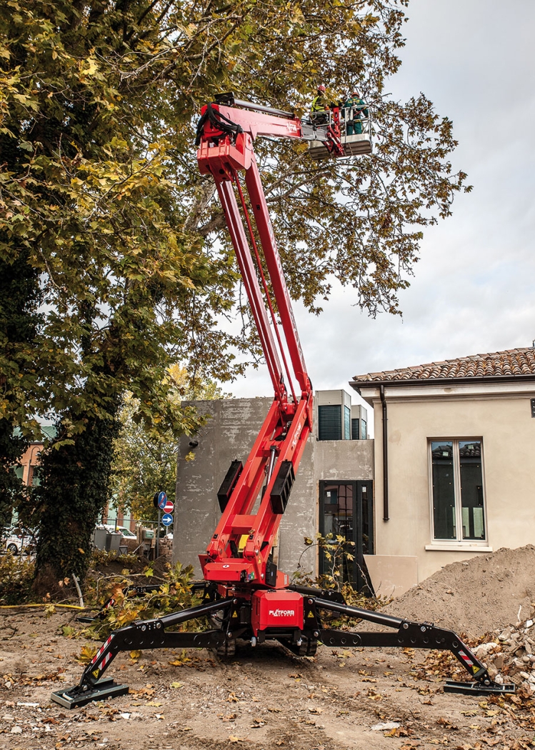 Spider lift fully extended near a small building.