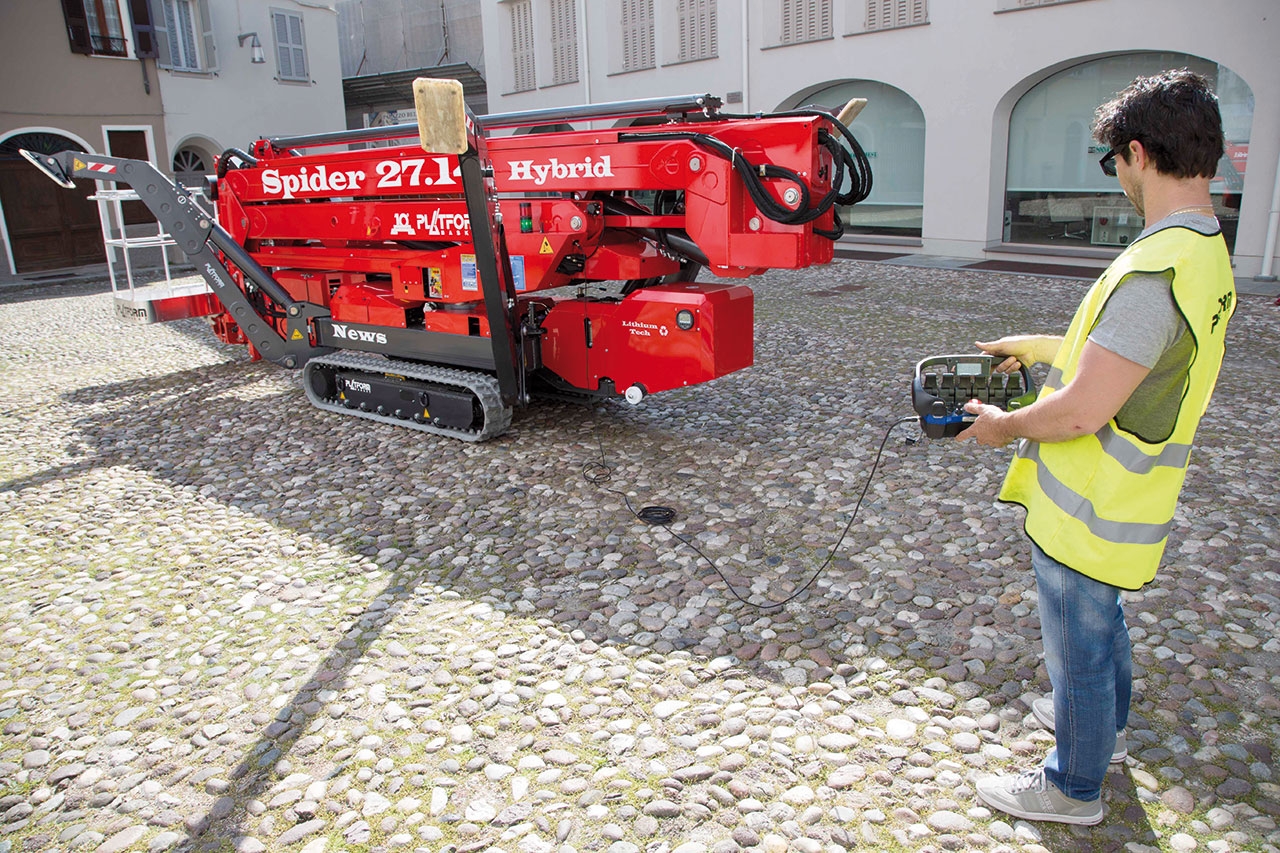 Worker operating a spider lift on a paved surface.